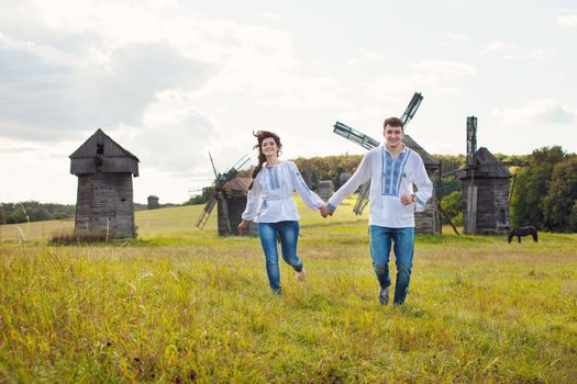 Happy young couple running on the field, against some old mills in the background