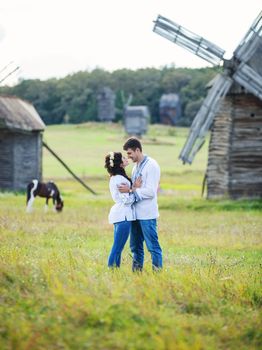 Young couple in Ukrainian traditional shirts on the field, old windmills in the background