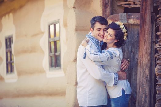 Young couple in Ukrainian style clothes standing at the entrance of rural house