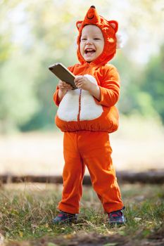 Joyful toddler boy in fox costume holding smartphone