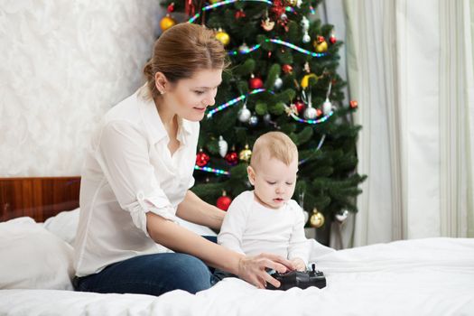 Young Caucasian mother and toddler son playing with RC controller against decorated Christmas tree at home