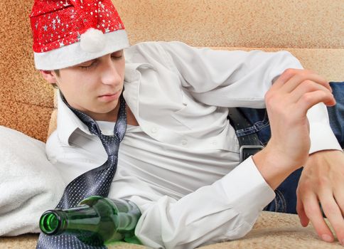 Drunken Teenager with Bottle of the Beer and Santa Hat on the Sofa at the Home