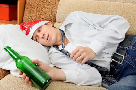 Drunken Teenager with Bottle of the Beer and Santa Hat on the Sofa at the Home