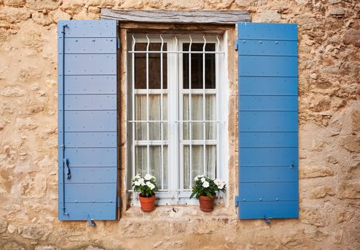 White Provence window with blue covers and pots of flowers in Grambois village, South France