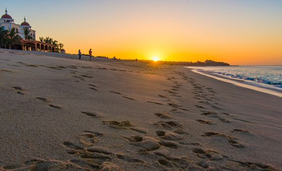 Sunrise on sandy beach with footsteps leading to distance