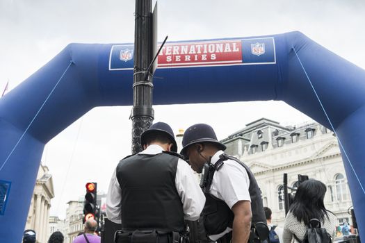 LONDON, UK - SEPTEMBER 27: British policemen standing next to inflatable NFL arch. September 27, 2014 in London. Regent street was closed to traffic to host NFL related games and events.