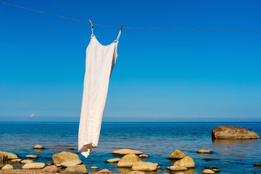 White dress hanging on a rope on the sea background