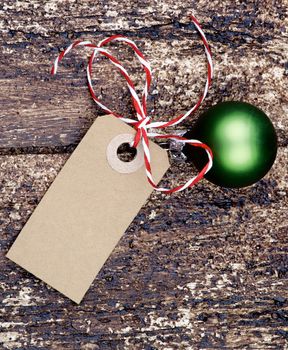 Christmas Decoration with Gift Card Note, Striped Bow and Green Bauble closeup on Textured Wooden background