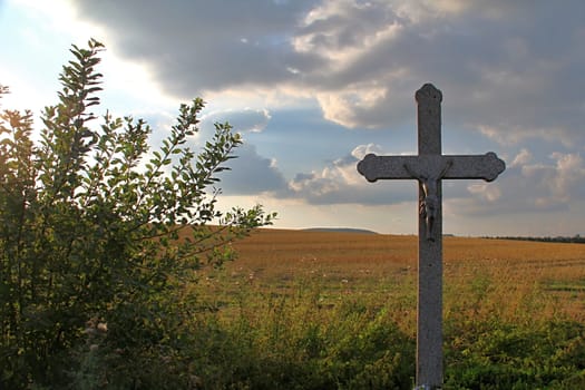 Photo shows details of countryside cross and landscape.