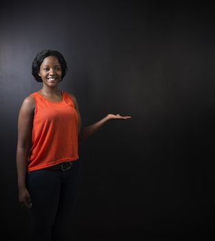 South African or African American woman teacher or student with hand out on chalk black board background
