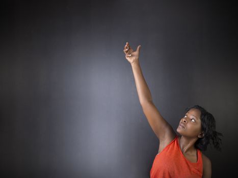 South African or African American woman teacher or student with hand reaching up on chalk black board background