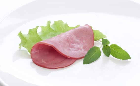 Beef sausage cut with green lettuce on the white plate