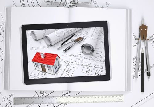 Small house with drawings displayed on tablet screen. Under the tablet lying open book and drawings with tools of architect. Construction concept