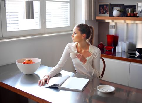 Relaxed woman drinking coffee in kitchen and looking out the window 