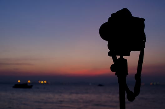 Silhouette of digital camera on tripod with sunset sky at sea blured background