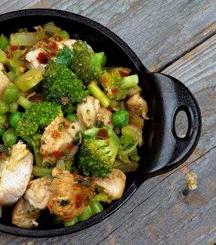 Homemade Chicken Stew with Broccoli, Bell Pepper and Green Pea in Black Saucepan closeup on Rustic Wooden background. Top View