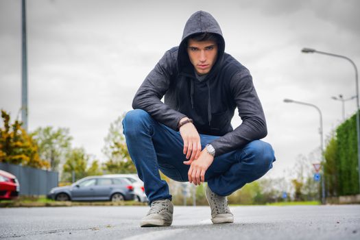 Attractive young man with hoodie and baseball cap in city street, looking at camera