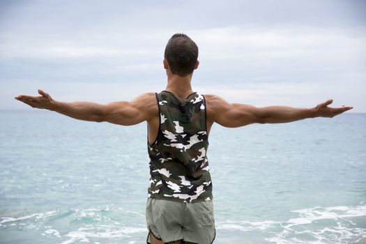 Muscular young man on the beach seen from the back, with arms open enjoying the sensation