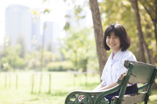 Schoolgirl sitting on the bench. Within the park. Girl smiling