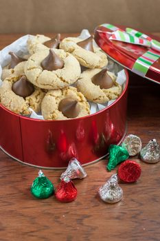 Preanut butter blossoms in a gift tin, highlighted with chocolate candies and and cookies on a wooden table.
