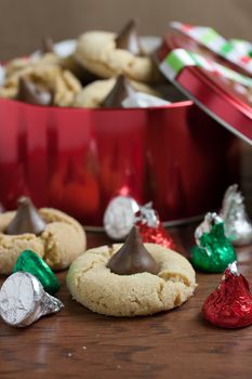 Preanut butter blossoms in a gift tin, highlighted with chocolate candies and and cookies on a wooden table.