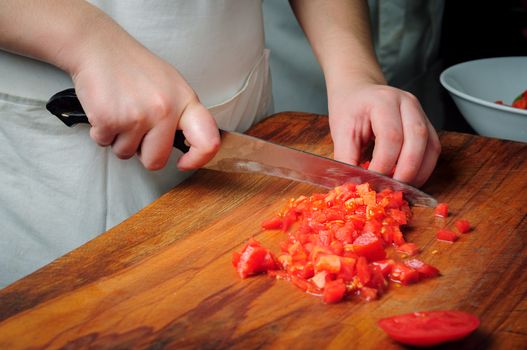 Chief slicing tomatoes on wooden board using knife 