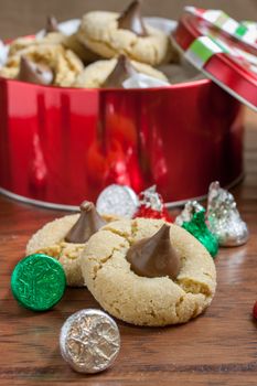 Preanut butter blossoms in a gift tin, highlighted with chocolate candies and and cookies on a wooden table.