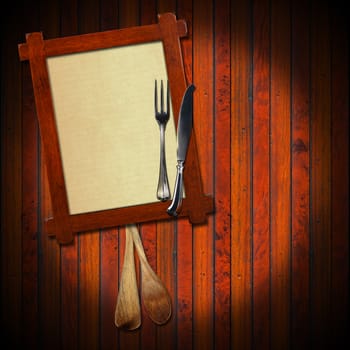 Wooden frame with a blank sheet of paper, two wooden spoons and silver cutlery on wooden background. Template for recipes or food menu

