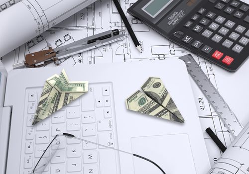 Paper airplanes of dollars lying on laptop keyboard. Architectural drawings and tools are close by. Concept of building business