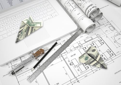 Paper airplanes of dollars lying on laptop keyboard and architectural drawings. Tools are close by. Concept of building business