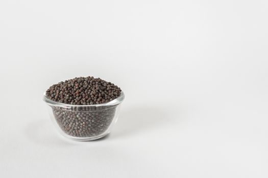 Dry black mustard seeds in a transparent glass bowl on white