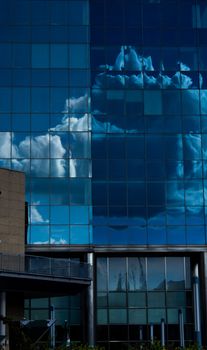 A modern glass building reflects like a mirror clouds on a blue sky