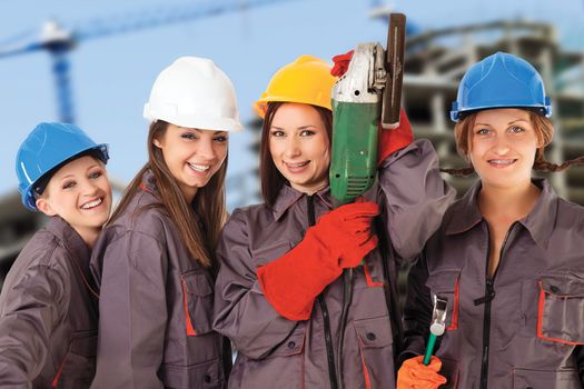 Four yung women wearing work clothes and helmets isolated with work path in front of a construction background.