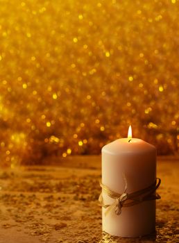Christmas decorative burning candle over golden bokeh background