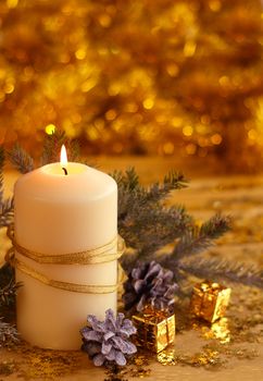 Christmas decorative burning candle, fir branch and decor over golden bokeh background