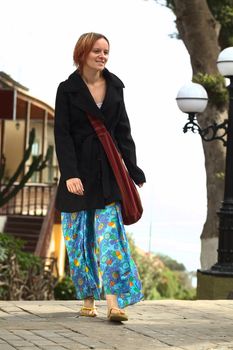 Young woman wearing colorful pants and a black coat walking on the street