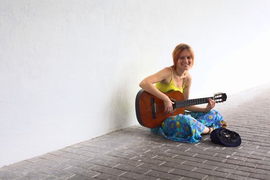 Young woman playing the guitar on the street with a hat containing some coins in front of her 