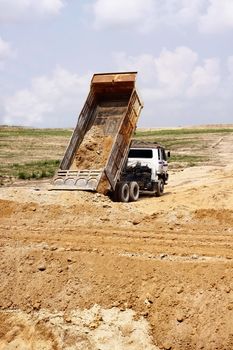 Heavy dump truck unloading soil on the sand at a construction site