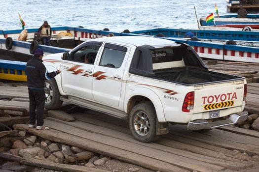 TIQUINA, BOLIVIA - OCTOBER 16, 2014: Toyota pickup truck driving onto a wooden ferry at the Strait of Tiquina at Lake Titicaca on October 16, 2014 in San Pedro de Tiquina, Bolivia. At the strait there is no bridge, the ferry is the only way to cross over to the other side.  