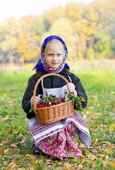 Little girl with a basket of berries of the mountain ash. Sunny autumn, sitting on the edge of the forest.