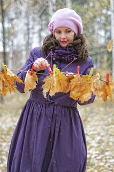 Girl hanging autumn leaves on the tree. It attaches clothespins.