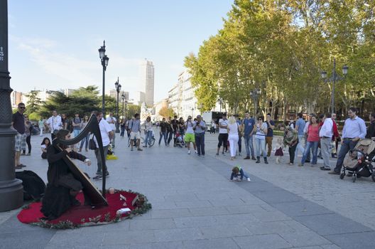 People watching a musician playing a harp in Bailen street, next to the Royal Palace in Madrid, Spain.