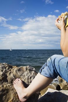 eating a sandwich at sea with foot placed on a rock.