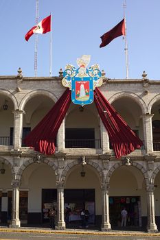 AREQUIPA, PERU - AUGUST 22, 2014: The city hall on Plaza de Armas (main square) with the coat of arms and red flag of Arequipa and the Peruvian banner on August 22, 2014 in Arequipa, Peru. The city center of Arequipa is UNESCO World Cultural Heritage Site.  