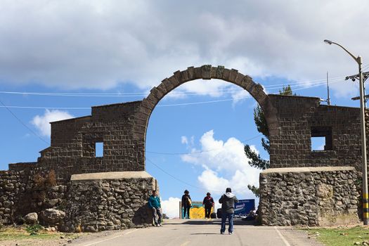YUNGUYO, PERU - OCTOBER 10, 2014: Unidentified people standing at the arch on the border between Yunguyo (Peru) and Kasani (Bolivia) photographed from the Peruvian side on October 10, 2014 in Yunguyo, Peru