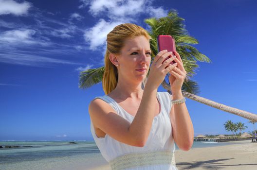 Young woman with cell phone on beach. Makes a Selfie with the smartphone. In the background  the tropical sea and blue sky.