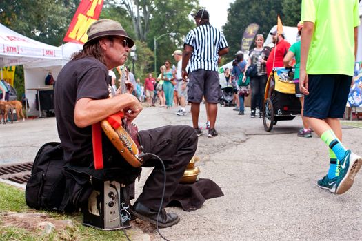 Atlanta, GA, USA - August 16, 2014:  A man strums a bass guitar for tips while sitting on the curb at the Piedmont Park Arts Festival.