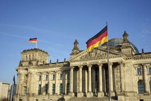 Frontal view of Reichstag building with German flag waving in a beautiful day with blue sky, Berlin, Germany, Europe.