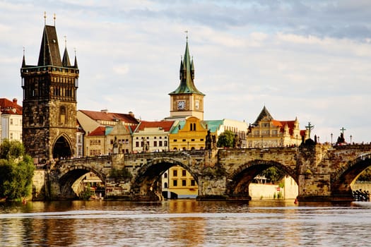 Photo shows the bridge, river and some old houses in Prague.