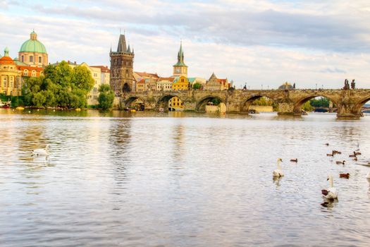 Photo shows the bridge, river and some old houses in Prague.